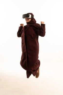 The use of modern and advanced technologies, digital transformation and technological progress, gestures of integration and focus in virtual reality, a portrait of a young Arab Gulf Saudi woman wearing a hijab and an abaya jumping in the air while wearing VR glasses, full-body, white background.