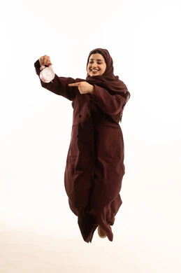 تنظيم الجدول الزمني، مفهوم ادارة الوقت, اداراك قيمة اللحظات الثمينة, بورتريه لشابة عربية خليجية سعودية محجبة ترتدي عباءة تقفز في الهواء تمسك بيدها الساعة وتنظر و تشير الية بإيماءات السرور والثقة بالنفس، الجسم بالطول الكامل، خلفية بيضاء