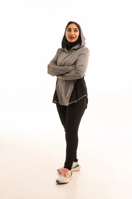 مفهوم الرشاقة واللياقة، انشطة بدنية نسائية، ايماءات السرور والسعادة، نمط حياة صحي ومفيد،تقوية العضلات ونحت الجسم، بورتريه لشابة عربية خليجية سعودية ترتدي زي رياضي شئ ما بايدي متقاطعة ، خلفية بيضاء