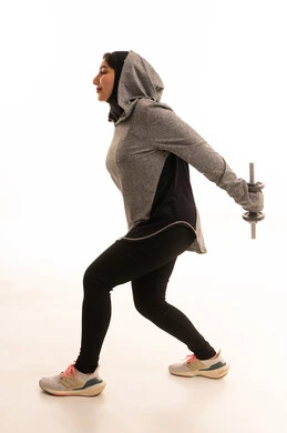 أسلوب حياة صحي،  بورتريه لفتاة عربية خليجية سعودية ترتدي الملابس الرياضية، ممارسة التمارين الرياضية مع الدمبل، نشاط بدني للمحافظة على الصحة واللياقة الجسدية، تمارين رفع الأثقال (دمبلز)، رفع الأوزان الحديدية الثقيلة، صورة بالطول الكامل، خلفية بيضاء