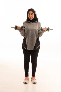 تمارين رفع الأثقال (دمبلز)، بورتريه لفتاة عربية خليجية سعودية ترتدي الملابس الرياضية، ممارسة التمارين الرياضية مع الدمبل، نشاط بدني للمحافظة على الصحة واللياقة الجسدية، أسلوب حياة صحي،   رفع الأوزان الحديدية الثقيلة، صورة بالطول الكامل، خلفية بيضاء