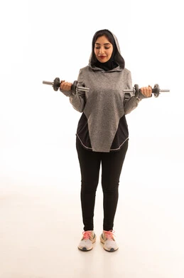 نشاط بدني للمحافظة على الصحة واللياقة الجسدية، بورتريه لفتاة عربية خليجية سعودية ترتدي الملابس الرياضية، ممارسة التمارين الرياضية مع الدمبل،  أسلوب حياة صحي، تمارين رفع الأثقال (دمبلز)، رفع الأوزان الحديدية الثقيلة، صورة بالطول الكامل، خلفية بيضاء