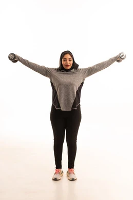 Exercising with dumbbells, a portrait of a Gulf Arab Saudi girl wearing sportswear, physical activity to maintain health and physical fitness, bodybuilding, a healthy lifestyle, muscle building, weightlifting exercises (dumbbells), lifting heavy weights, full-length image, white background.