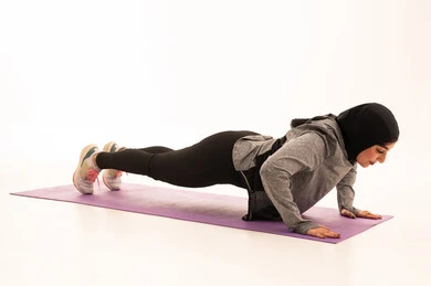 إيماءات الحماس و النشاط، المحافظة على التوازن الجسدي، نمط حياة صحي ومفيد، ممارسة التمرينات الأرضية لشد الجسد، مفهوم الرشاقة واللياقة، انشطة بدنية نسائية، تقوية العضلات ونحت الجسم، بورتريه لشابة عربية خليجية سعودية ترتدي زي رياضي تقوم بممارسة التمرينات الرياضية ، خلفية بيضاء