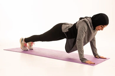 Maintaining physical balance, a healthy and beneficial lifestyle, practicing ground exercises to tone the body, the concept of agility and fitness, women's physical activities, strengthening muscles and sculpting the body, a portrait of a young Arab Gulf Saudi woman wearing sportswear exercising, gestures of enthusiasm and activity, white background.