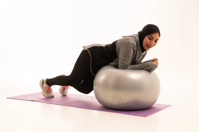 Healthy lifestyle, a Gulf Arab Saudi girl wearing sportswear, exercising with a fitness ball, physical activity to maintain health and physical fitness, practicing Pilates ball exercises and balance, white background.