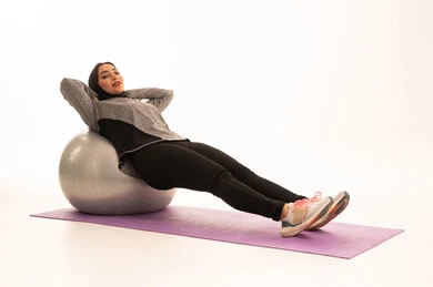 A Saudi Arabian Gulf girl wearing sportswear, exercising with a fitness ball, a physical activity to maintain health and physical fitness, a healthy lifestyle, practicing Pilates ball and balance exercises, white background.