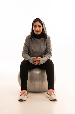 Physical activity to maintain health and physical fitness, an Arab Gulf Saudi girl wearing sportswear, exercising with a fitness ball, a healthy lifestyle, practicing Pilates ball and balance exercises, white background.