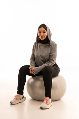 Practicing Pilates ball and balance exercises, an Arab Gulf Saudi girl wearing sportswear, exercising with a fitness ball, physical activity to maintain health and physical fitness, a healthy lifestyle, white background.