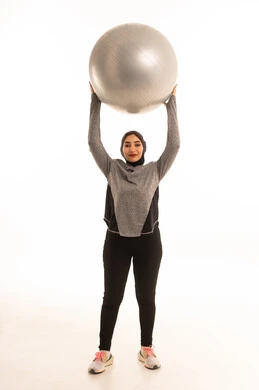 A Saudi Arabian Gulf girl wearing sportswear, exercising with a fitness ball, a physical activity to maintain health and physical fitness, a healthy lifestyle, practicing Pilates ball and balance exercises, white background.