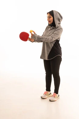 انشطة ترفيهية ممتعه ، اللعب بسرعة وتركيز،  بورتريه  لشابة عربية خليجية سعودية ترتدي ملابس رياضية تحمل بيدها مضرب تنس الطاولة، المحافظة على الرياضة والرشاقة الجسدية، خلفية بيضاء