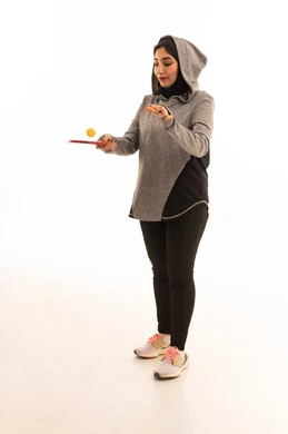 بورتريه  لشابة عربية خليجية سعودية ترتدي ملابس رياضية تحمل بيدها مضرب تنس الطاولة، المحافظة على الرياضة والرشاقة الجسدية، اللعب بسرعة وتركيز، ممارسة رياضات وانشطة بدنية ممتعة، خلفية بيضاء