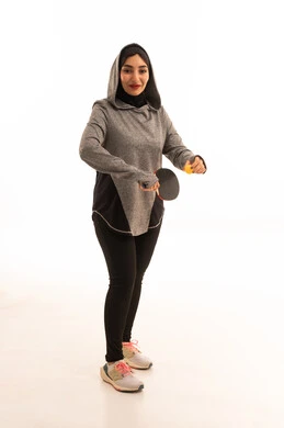 اللعب بسرعة وتركيز، ممارسة رياضات وانشطة بدنية ممتعة، بورتريه  لشابة عربية خليجية سعودية ترتدي ملابس رياضية تحمل بيدها مضرب تنس الطاولة، المحافظة على الرياضة والرشاقة الجسدية، خلفية بيضاء