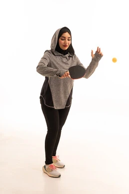 Playing with speed and focus, practicing fun sports and physical activities, a portrait of a young Arab Gulf Saudi woman wearing sportswear holding a table tennis racket in her hand, maintaining sports and physical fitness, white background.