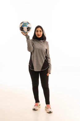 احتراف الرياضات الجماعية، النظر إلى الكاميرا بإيماءات السعادة بالفوز والنصر، المحافظة على نمط حياة صحي، بورتريه  للاعبة عربية خليجية سعودية محجبة مبتسمة ترتدي الملابس الرياضية تحمل كرة القدم وكأس البطولة، خلفية بيضاء