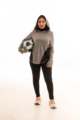 Passion for sports, looking at the camera with gestures of happiness for victory and success, professionalism in team sports, maintaining a healthy lifestyle, a portrait of a smiling Saudi Arabian Gulf female player wearing sportswear and holding a football, white background.