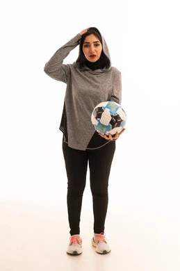 احتراف الرياضات الجماعية، النظر إلى الكاميرا بإيماءات الهزيمة، المحافظة على نمط حياة صحي، بورتريه مقرب للاعبة عربية خليجية سعودية محجبة مبتسمة ترتدي الملابس الرياضية تحمل كرة القدم وكأس البطولة، خلفية بيضاء