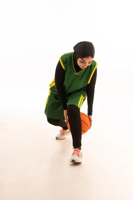 الشغف بالألعاب الرياضية , ممارسة هواية كرة السلة , بورتريه لامرأة عربية خليجية سعودية ترتدي ملابس رياضية تلعب بالكرة بإيماءات التشجيع و الحماس , الفريق السعودي النسائي , صورة للجسم بالكامل ،خلفية بيضاء