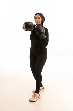 Maintaining physical fitness, increasing muscle endurance, a portrait of a Saudi Gulf Arab girl wearing sportswear and gloves looking at the camera learning the arts of boxing, training in combat movements, enhancing bone and joint health, white background.