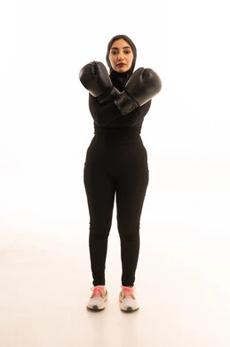 تعزيز صحة العظام والمفاصل،المحافظة على اللياقة البدنية،المحافظة على اللياقة البدنيةر، زيادة قدرة العضلات على التحمل، بورتريه لفتاة عربية خليجية سعودية ترتدي الملابس الرياضية والقفازات تنظر إلى الكاميرا تتعلم فنون الملاكمة، التدرب على الحركات القتالية ، خلفية بيضاء