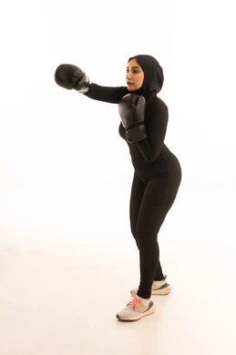 Increasing muscle endurance, maintaining physical fitness, a portrait of a Saudi Gulf Arab girl wearing sportswear and gloves looking at the camera learning the arts of boxing, training in combat movements, white background, enhancing bone and joint health, enhancing health.