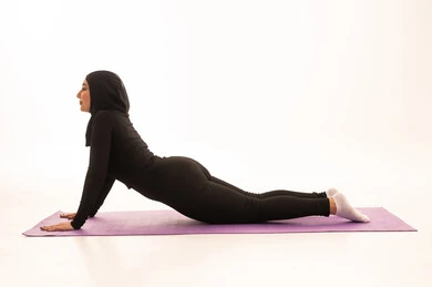 Gestures of enthusiasm and activity, maintaining physical balance, a healthy and beneficial lifestyle, practicing floor exercises to tone the body, the concept of agility and fitness, women's physical activities, strengthening muscles and sculpting the body, a portrait of a young Arab Gulf Saudi woman wearing sportswear exercising, white background.