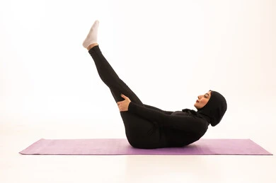 Maintaining physical balance, a healthy and beneficial lifestyle, practicing ground exercises to tone the body, the concept of agility and fitness, women's physical activities, strengthening muscles and sculpting the body, a portrait of a young Arab Gulf Saudi woman wearing sportswear exercising, gestures of enthusiasm and activity, white background.