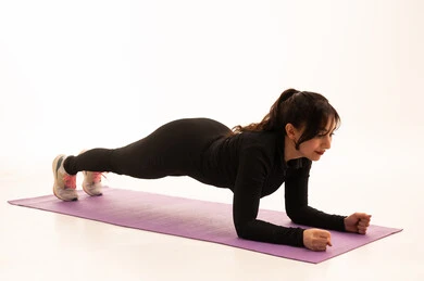A healthy and beneficial lifestyle, maintaining physical balance, practicing ground exercises to tone the body, the concept of agility and fitness, women's physical activities, strengthening muscles and sculpting the body, a portrait of a young Arab Gulf Saudi woman wearing sportswear exercising, gestures of enthusiasm and activity, white background.