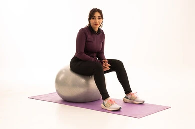 A Saudi Arabian Gulf girl, wearing sportswear, exercising with a fitness ball, a physical activity to maintain health and physical fitness, a healthy lifestyle, practicing Pilates ball and balance exercises, white background.