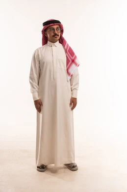 الوقوف باستقامة والنظر إلى شيء ما ، الاهتمام بالمظهر الخارجي والأناقة، بورتريه  لرجل عربي خليجي سعودي يرتدي الثوب والشماغ التقليدي ويضع نظارات طبية، مفهوم الرجولة والخشونة، صورة الجسم بالطول الكامل، خلفية بيضاء