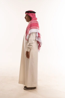 مفهوم الرجولة والخشونة، الاهتمام بالمظهر الخارجي والأناقة، ايماءات وجه و ابتسامة تأمل و سرور, الوقوف باستقامة والنظر نحو إلى شيء ما ، بورتريه  لرجل عربي خليجي سعودي يرتدي الثوب التقليدي والشماغ ويضع ، شاب سعودي يرتدي نظارات طبية، صورة الجسم بالطول الكامل، خلفية بيضاء