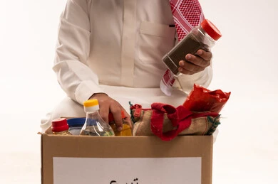 جمعية خيرية ومبادرة انسانية، الانفاق والتبرع في سبيل الله للجمعيات السعودية، التصدق بالفائض من المستلزمات، أنواع المواد غذائية، بورتريه مقرب لرجل خليجي عربي سعودي يرتدي الثوب التقليدي والشماغ يحمل بيده صندوق التبرعات ويمسك مواد غذائية، خلفية بيضاء