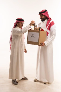 Project to feed the needy, providing a food basket, the concept of assistance and donation, food items for donation and bringing joy to the hearts of children, participating in rewards, Islamic charities in Saudi Arabia, helping to provide basic needs, portrait of two Arab Gulf men from Saudi Arabia, white background.