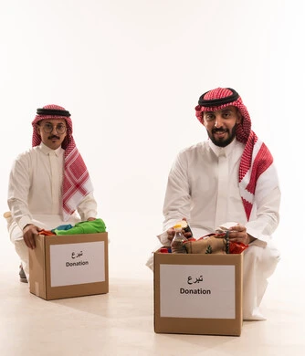 تقسيم المحتويات بين مواد غذائية وملابس، بورتريه لرجلان خليجيان عربيان سعوديان يقومان بتجهيز صندوق المواد الغذائية، التبرع لمشروع السلة الغذائية، توفير الطعام للمحتاجين، مبادرات وتبرعات انسانية خيرية، جمعيات اسلامية في السعودية، شهر رمضان، خلفية بيضاء