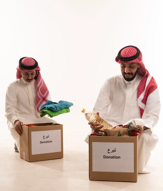 Donating to the food basket project, Islamic charities in Saudi Arabia, distributing prepared rations, a portrait of two Gulf Arab Saudi men preparing a food and clothing box, providing food for the needy, humanitarian charitable initiatives and donations, the month of Ramadan, white background.