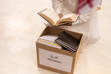 الأعمال الصالحة في أقات فضيلة، التبرع  والانفاق في سبيل الله للجمعيات، تعابير الاندماج والتركيز، جمعية خيرية ومبادرة انسانية، التصدق بالفائض من المستلزمات،  بورتريه مقرب لرجل  خليجي عربي سعودي يرتدي الثوب التقليدي والشماغ يحمل بيده كتاب ويقرأه، خلفية بيضاء