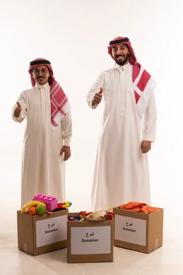 Signal of approval and acceptance, donating to the project of feeding the hungry, children's toys for donation and bringing joy to the little ones, Islamic charities in Saudi Arabia, helping to provide needs, a portrait of two Gulf Arab Saudi men preparing a donation box, distributing prepared meals, white background.