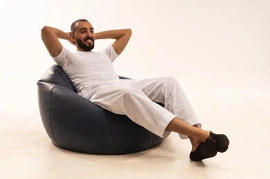 الاهتمام بالمظهر الخارجي، مفهوم الأناقة والاهتمام بالمظهر الخارجي، التأمل والتخطيط للمستقبل، شاب سعودي مبتسم، إيماءات التذكر والشرود، مفهوم الجلوس والراحة، بورتريه مقرب لرجل عربي خليجي سعودي مبتسم يرتدي سروال وفانيلا باللون أبيض يجلس على كرسي مريح يضع يداه خلف رأسه، خلفية بيضاء