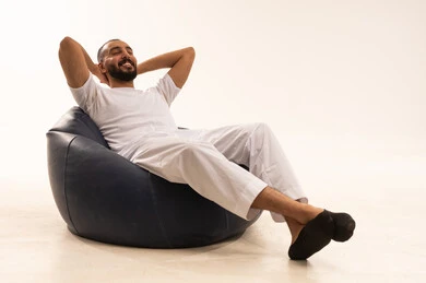 Contemplation and planning for the future, concern for external appearance, the concept of elegance and attention to external appearance, a smiling Saudi young man, gestures of remembrance and distraction, the concept of sitting and relaxation, a close-up portrait of a smiling Arab Gulf Saudi man wearing white pants and a t-shirt sitting on a comfortable chair with his hands behind his head, white background.