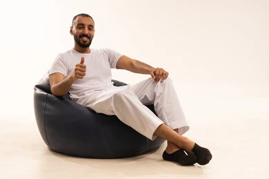 مفهوم الأناقة والاهتمام بالمظهر الخارجي، التأمل والتخطيط للمستقبل، الاهتمام بالمظهر الخارجي،  شاب سعودي مبتسم، إيماءات التذكر والشرود، مفهوم الجلوس والراحة، بورتريه مقرب لرجل عربي خليجي سعودي مبتسم يرتدي سروال وفانيلا باللون أبيض يجلس على كرسي مريح يشير بالموافقة، خلفية بيضاء