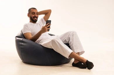 انجاز المهام اليومية على أجهزة متطورة وحديثة ، استخدام اجهزة تقنية حديثة، إجراء مكالمات الفيديو عبر الانترنت، بورتريه  لرجل عربي سعودي خليجي يرتدي سروال وفانيلا باللون أبيض يجلس على كرسي مريح ويحمل جهاز الحاسب المحمول ، مفهوم الرجولة والثقة بالنفس،  خلفية بيضاء