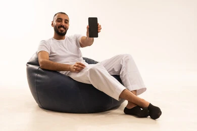 A black screen on a mobile device, using modern technology devices, making video calls over the internet, a portrait of an Arab Saudi Gulf man wearing white pants and a t-shirt sitting on a comfortable chair holding a mobile phone, the concept of masculinity and self-confidence, white background.
