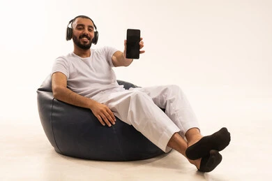 A display of a black screen background, using modern technology devices, browsing social media, making video calls over the internet, a portrait of an Arab Saudi Gulf man wearing white pants and a t-shirt sitting on a comfortable chair holding a mobile phone, the concept of masculinity and self-confidence, white background.