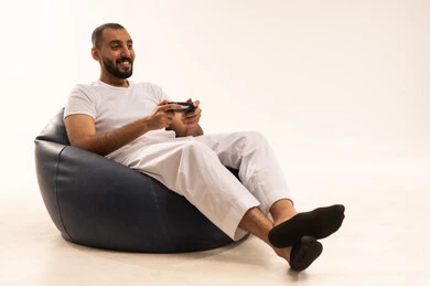 التفاعل والاندماج مع ألعاب البلايستيشن، قضاء وقت ممتع ومسلي، تعابير فوز وخسارة، تقنيات الكترونية حديثة ترفيهيه, بورتريه  لرجل عربي سعودي خليجي يرتدي سروال وفانيلا باللون الأبيض يجلس على كرسي مريح يحمل بيده عصا التحكم يقوم باللعب في ألعاب الفيديو، خلفية بيضاء