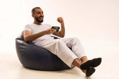 Spending enjoyable and entertaining time, interacting and engaging with PlayStation games, expressions of victory with a raised fist, modern electronic entertainment technologies, a close-up portrait of an Arab Saudi Gulf man wearing white pants and a t-shirt sitting on a comfortable chair holding a game controller playing video games, white background.