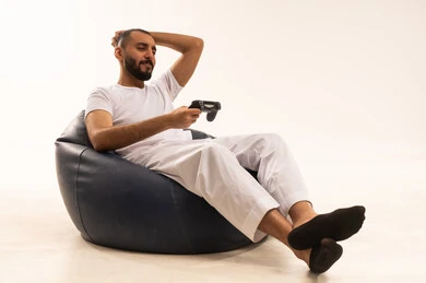 Expressions of winning and losing, interaction and immersion with PlayStation games, having a fun and entertaining time, modern electronic entertainment technologies, a portrait of an Arab Saudi Gulf man wearing white pants and a t-shirt sitting on a comfortable chair holding a game controller playing video games, white background.