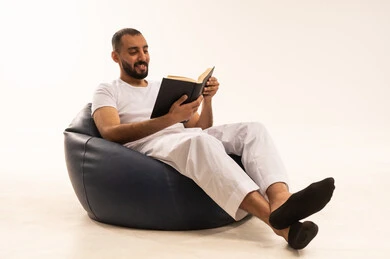 تصفح وتقليب الصفحات، قضاء وقت الفراغ بالتعلم والثقافة، مفهوم محو الامية، تعابير الاندماج والتركيز، هواية حب المطالعة والاستكشاف, بورتريه لرجل عربي خليجي سعودي يرتدي سروال وفانيلا باللون الأبيض يجلس على كرسي مريح يحمل بيده كتاب علمي تثقيفي وينظر الى شيء ما، خلفية بيضاء