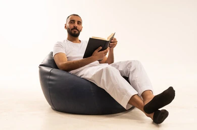 تعابير التأمل والاندماج،تصفح وتقليب الصفحات، قضاء وقت الفراغ بالتعلم والثقافة، مفهوم محو الامية، هواية حب المطالعة والاستكشاف, بورتريه لرجل عربي خليجي سعودي يرتدي سروال وفانيلا باللون الأبيض يجلس على كرسي مريح يحمل بيده كتاب علمي تثقيفي وينظر الى شيء ما، خلفية بيضاء