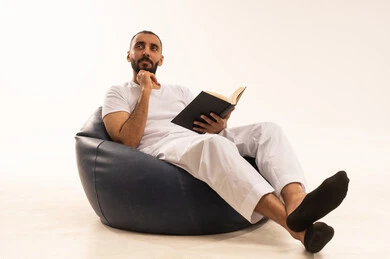 Spending free time on learning and culture, the concept of literacy, expressions of integration and focus, the hobby of reading and exploration, a portrait of an Arab Gulf Saudi man wearing white pants and a t-shirt sitting on a comfortable chair holding a scientific educational book and looking at something, white background.