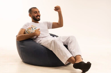 مشاهدة ومتابعة مباراة كرة القدم ، تنمية الهوايات الرياضية، إيماءات الشغف والتشجيع للفريق ، بورتريه لرجل عربي خليجي سعودي مبتسم يرتدي سروال وفانيلا باللون الأبيض يجلس على كرسي مريح يحمل الكرة ، الحماس والتفاعل مع المنتخب ، أنديه رياضية مختلفة، خلفية بيضاء .